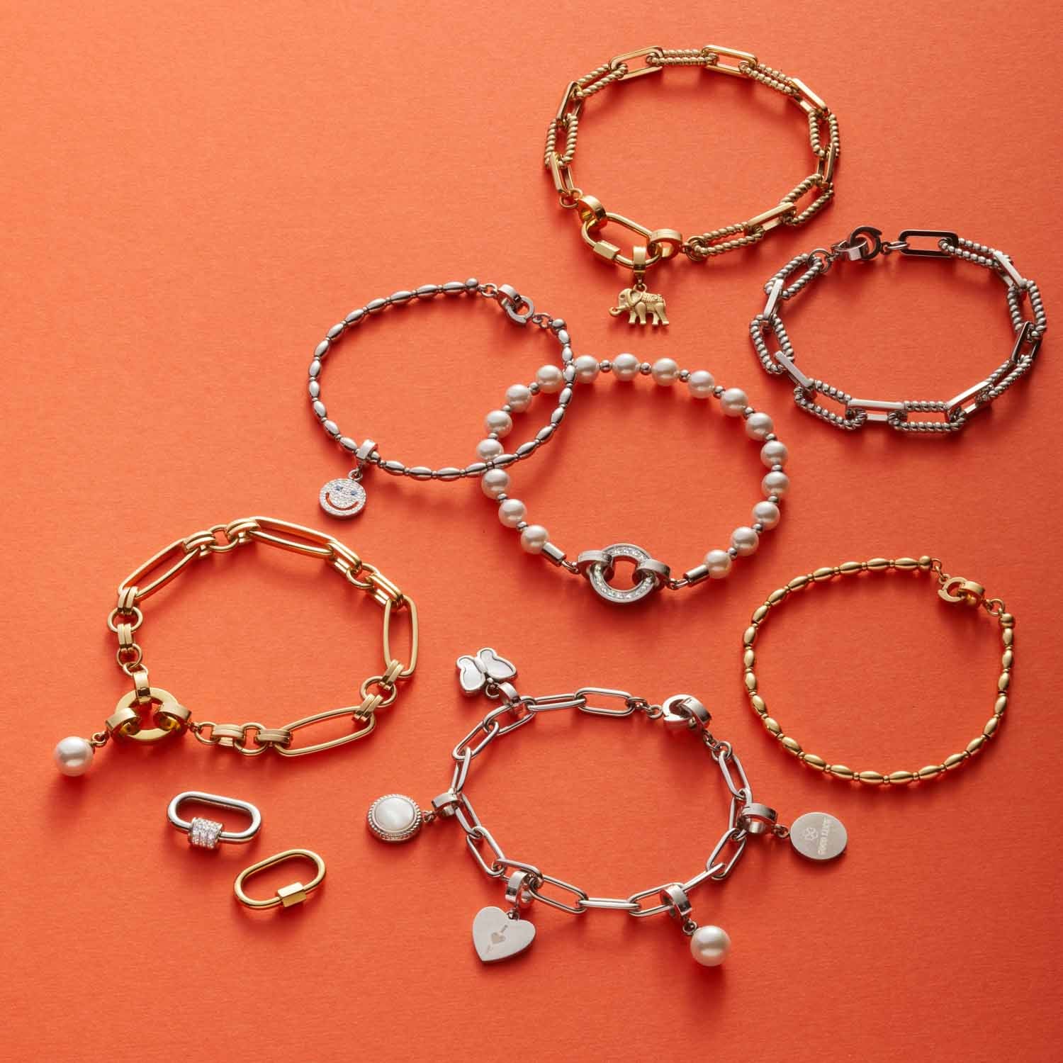 Mehrere gold- und silberfarbene Armbänder mit verschiedenen Anhängern auf orangem Hintergrund