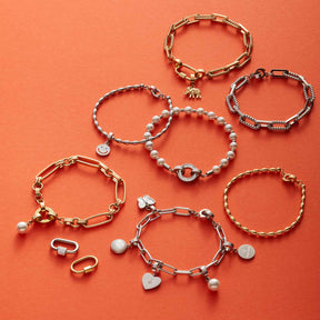 Mehrere gold- und silberfarbene Armbänder mit verschiedenen Anhängern auf orangem Hintergrund