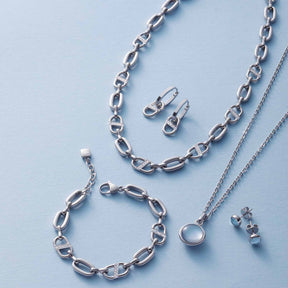 Silberne Armbänder und Halsketten der Serie NAREA mit Kettengliedern und Ohrringen auf hellem Untergrund