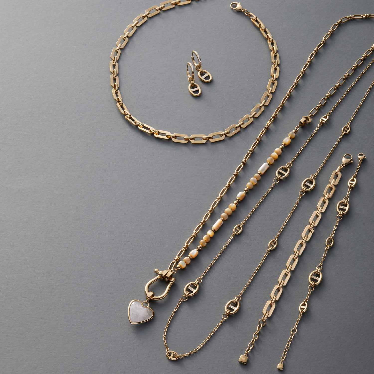 Creole HERMA gold mit verschiedenen Ketten und Ohringen auf grauem Untergrund