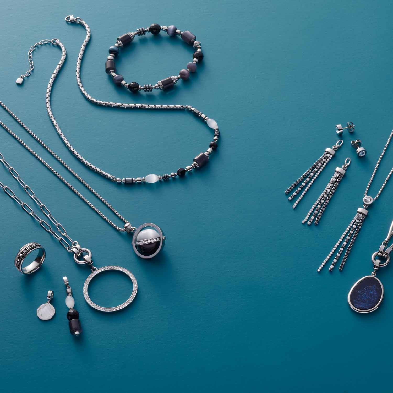 Schmuck-Kollektion auf blauem Hintergrund, silberne Halsketten, Armbänder, Ringe und Ohrringe mit Glassteinen