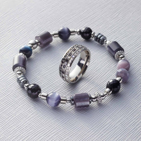 Armband CASORIA silber mit Glasperlen in Lila- und Schwarztönen neben Ring auf hellem Untergrund