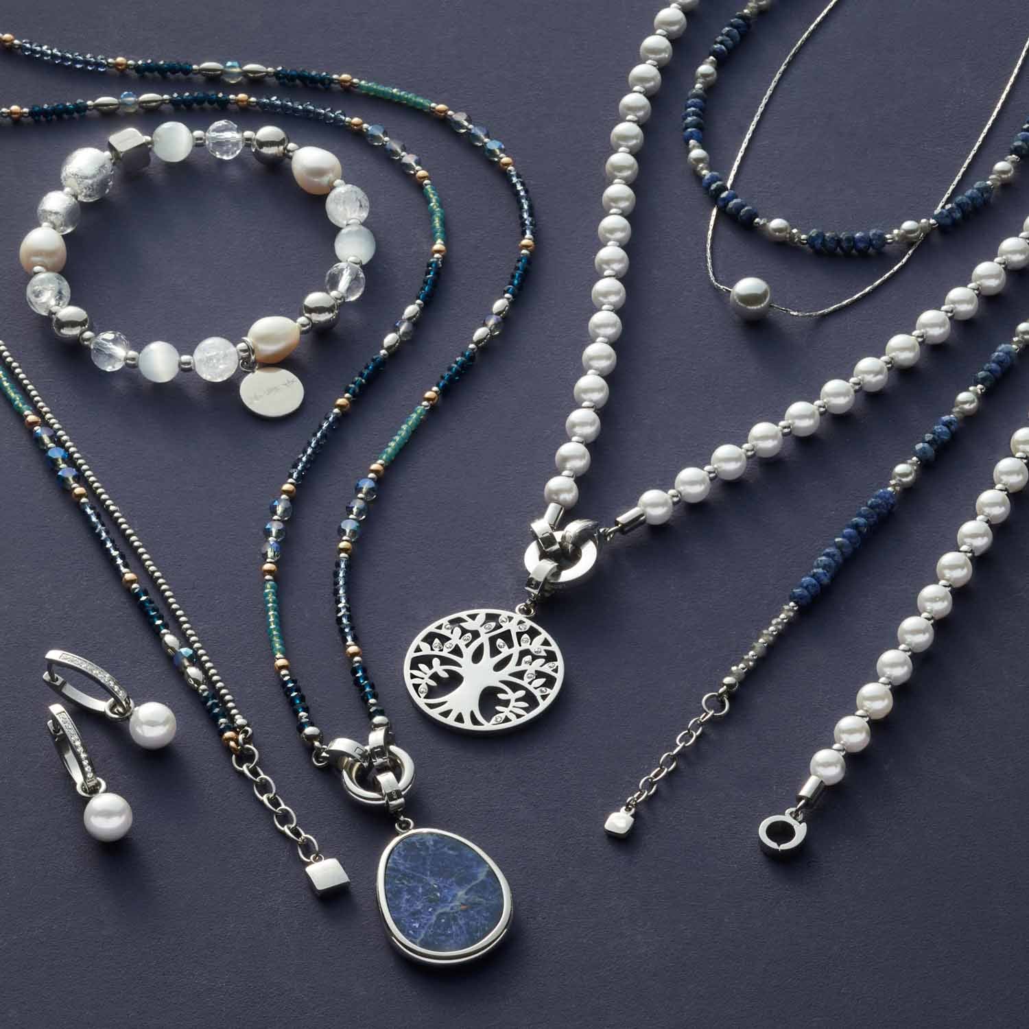 Schmuckkollektion mit Armbändern, Ketten und Ohrringen in Silber, Perlen und Sodalith auf grauem Untergrund