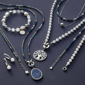 Schmuckkollektion mit Armbändern, Ketten und Ohrringen in Silber, Perlen und Sodalith auf grauem Untergrund