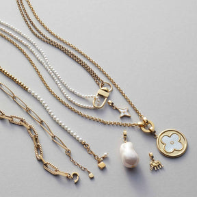 Mehrere Halsketten LUCINDA in Gold mit Perlen, Muscheln und Anhängern auf grauem Untergrund