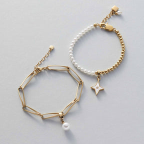 Zwei goldene Armbänder LUCINDA mit Perlen und Stern-Anhänger auf grauem Untergrund