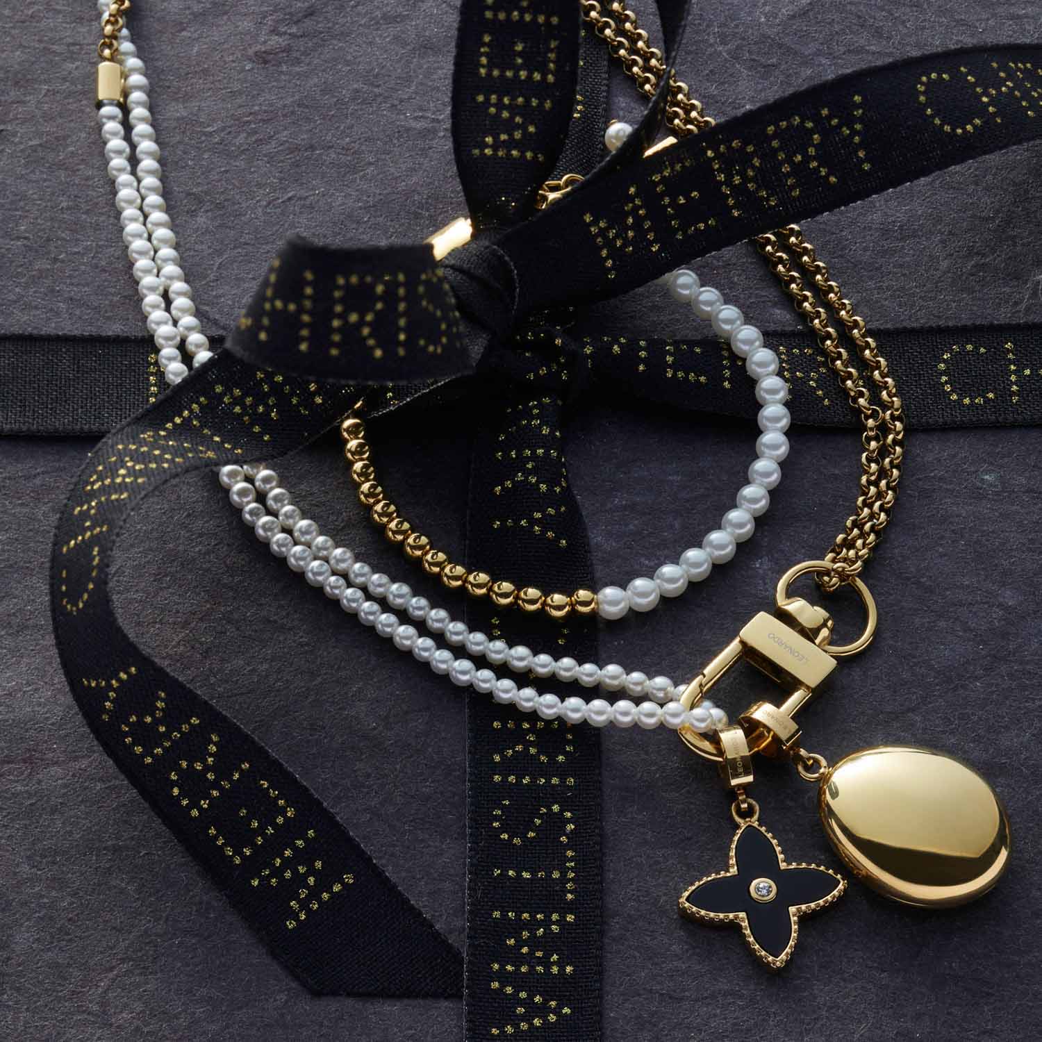 Armband LUCINDA gold mit Perlen, Muscheln und schwarzem Band auf grauem Untergrund