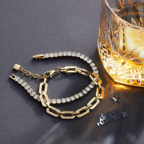 Armband CREMONA gold mit Glaskristallen und Kettengliedern neben Whiskeyglas auf grauem Untergrund
