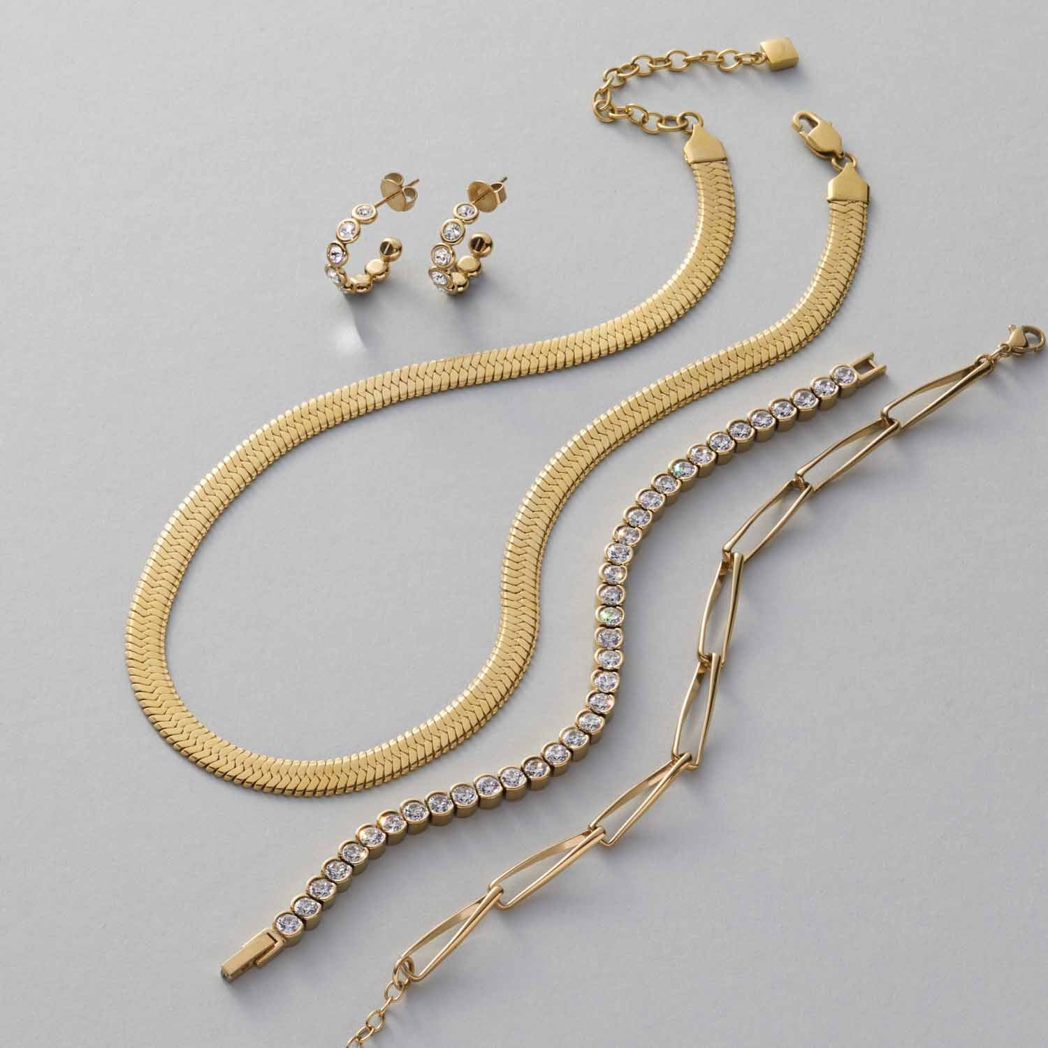 Goldene Schmuckkollektion mit Ohrringen, Ketten und Armbändern auf grauem Untergrund