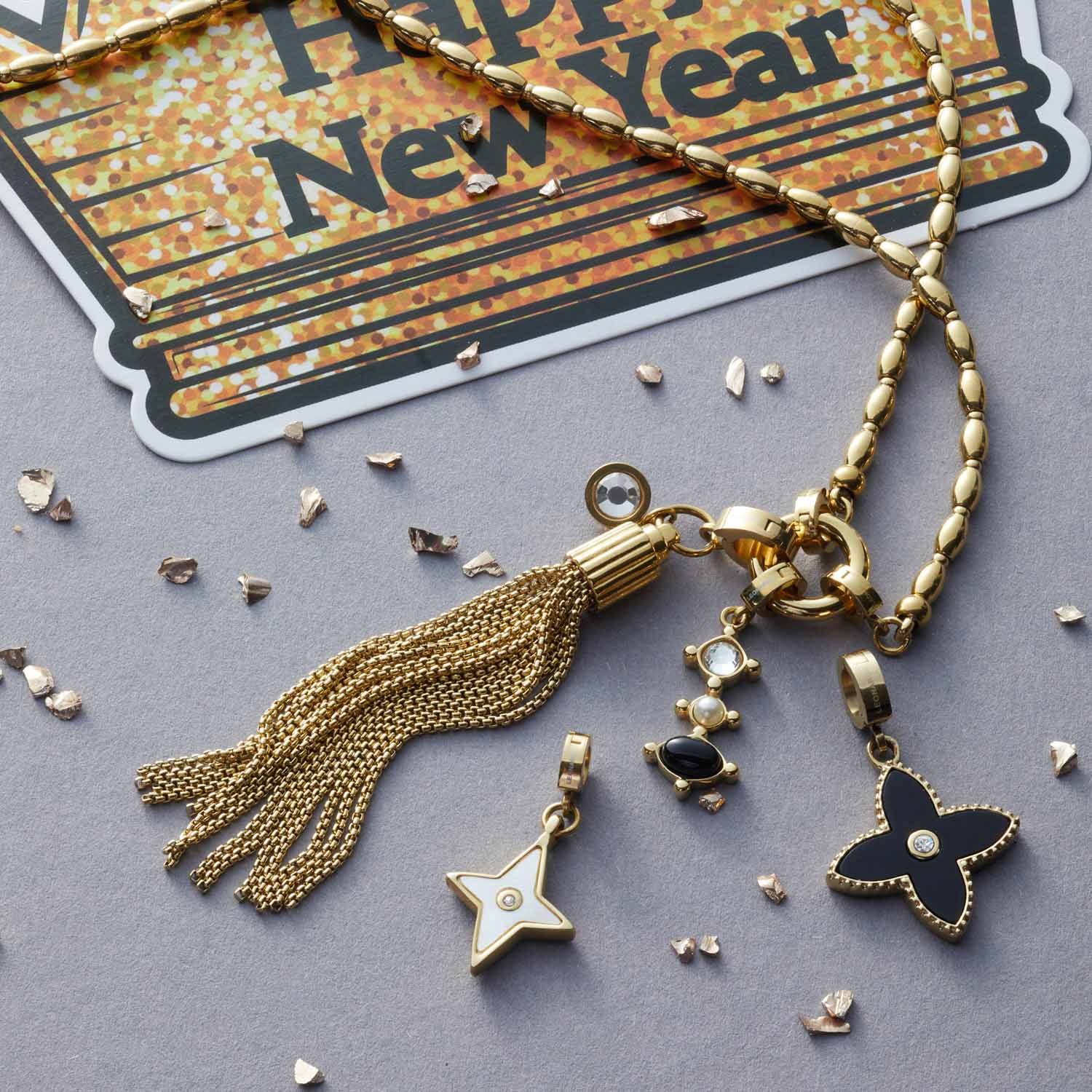 Anhänger PIETRA gold Clip & Mix mit Quaste und Charms auf grauem Untergrund