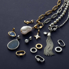 Schmuckkollektion mit goldenem Anhänger WILMA, Ketten, Ringen und Perlendetails auf grauem Hintergrund