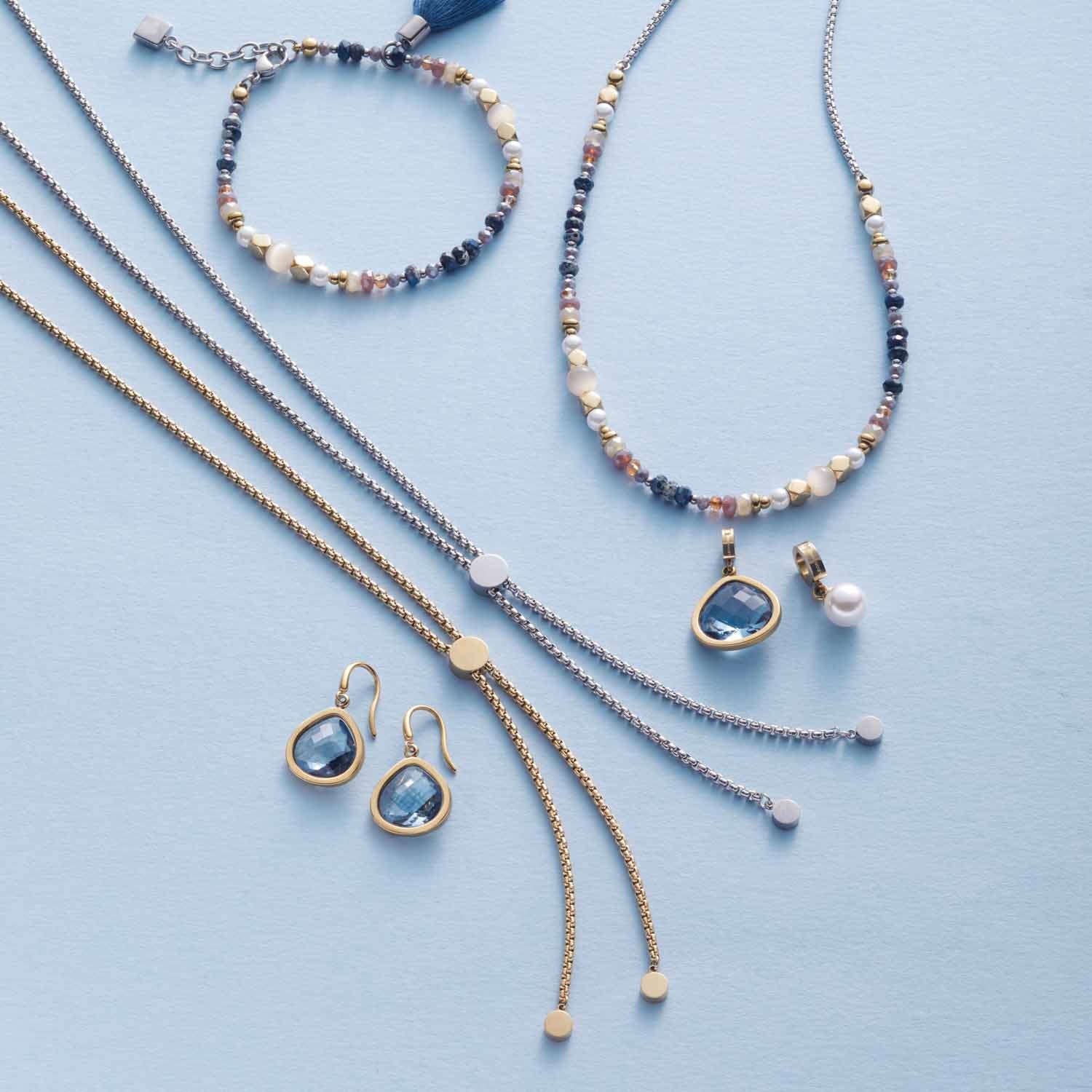 Ohrhänger JUVINGA gold mit Glasperlen, Halsketten und Armband auf hellblauem Hintergrund