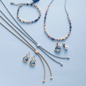 Ohrhänger JUVINGA gold mit Glasperlen, Halsketten und Armband auf hellblauem Hintergrund