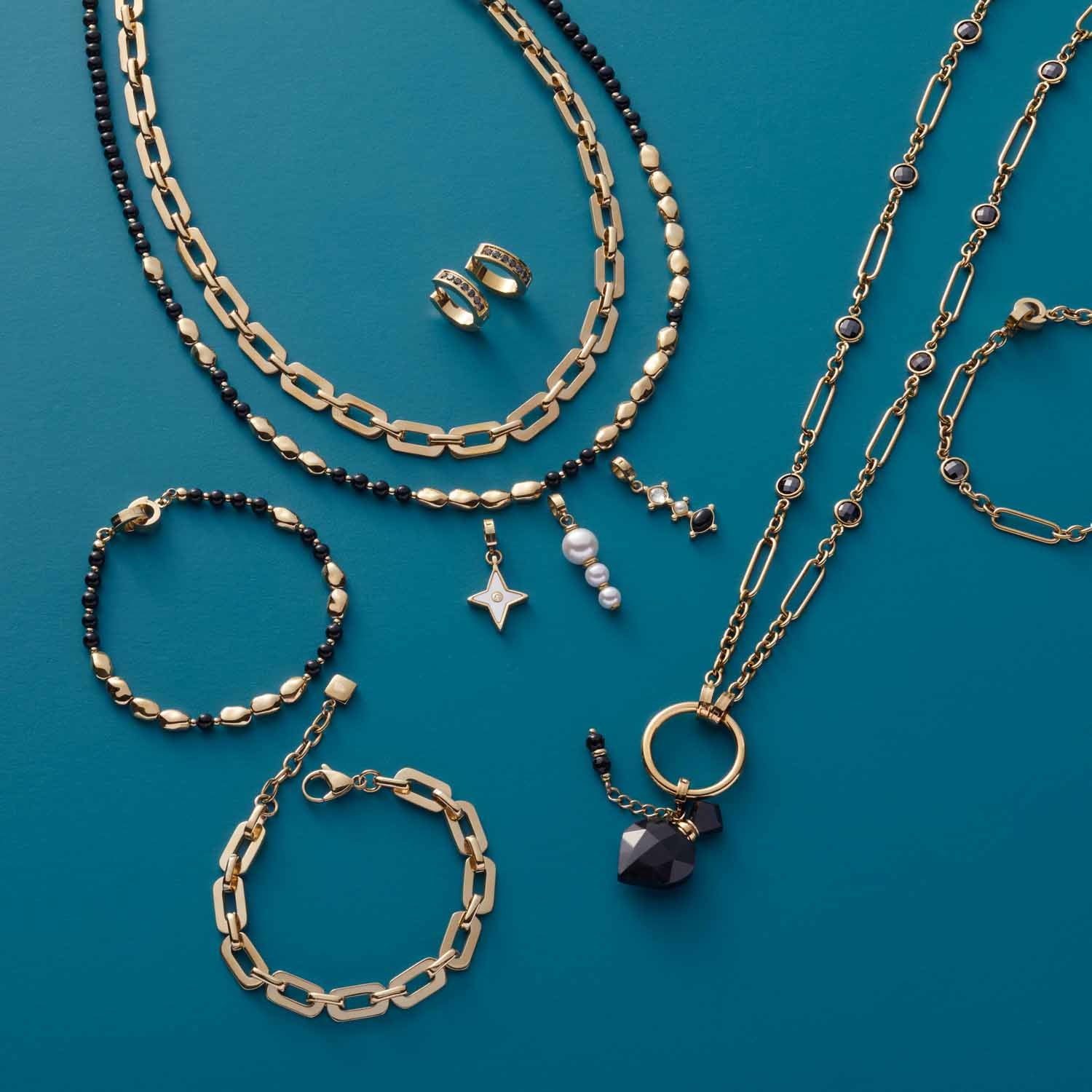 Schmuckkollektion mit Armbändern, Ketten und Ohrringen in Gold und Schwarz auf türkisblauem Hintergrund