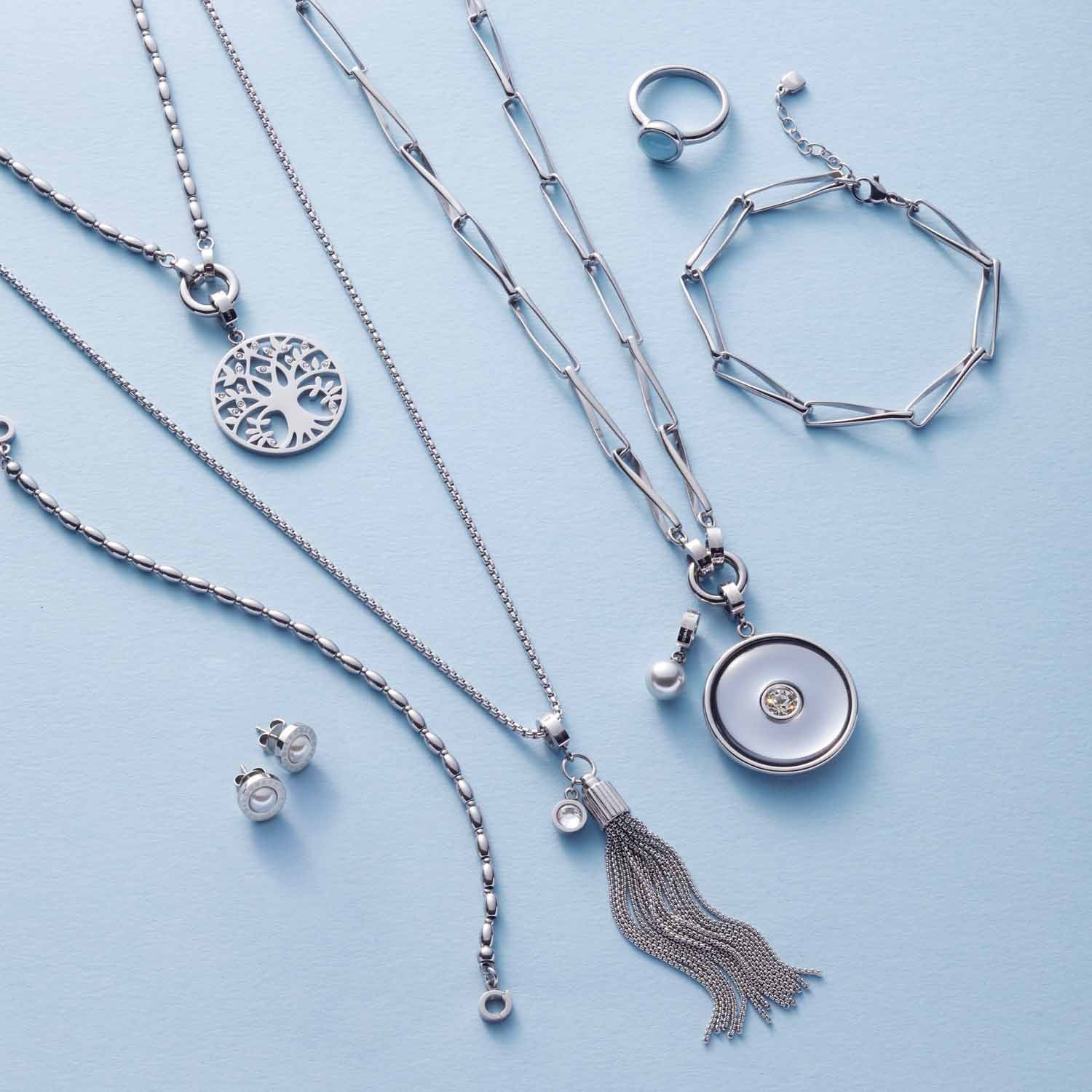 Silberner Schmuck aus der Serie CONSENZA auf hellblauem Hintergrund: Armbänder, Halsketten, Ring und Ohrstecker