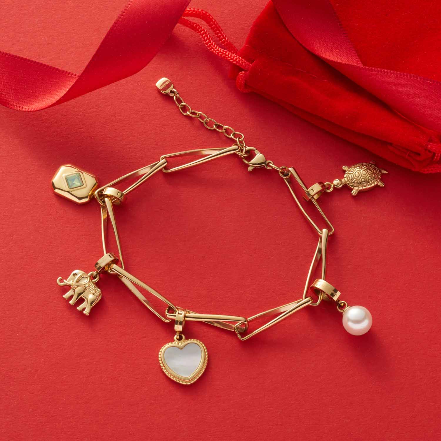 Armband CONSENZA gold mit Charms auf rotem Hintergrund