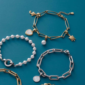 Armband CONSENZA gold mit weiteren Schmuckstücken auf türkisfarbenem Hintergrund