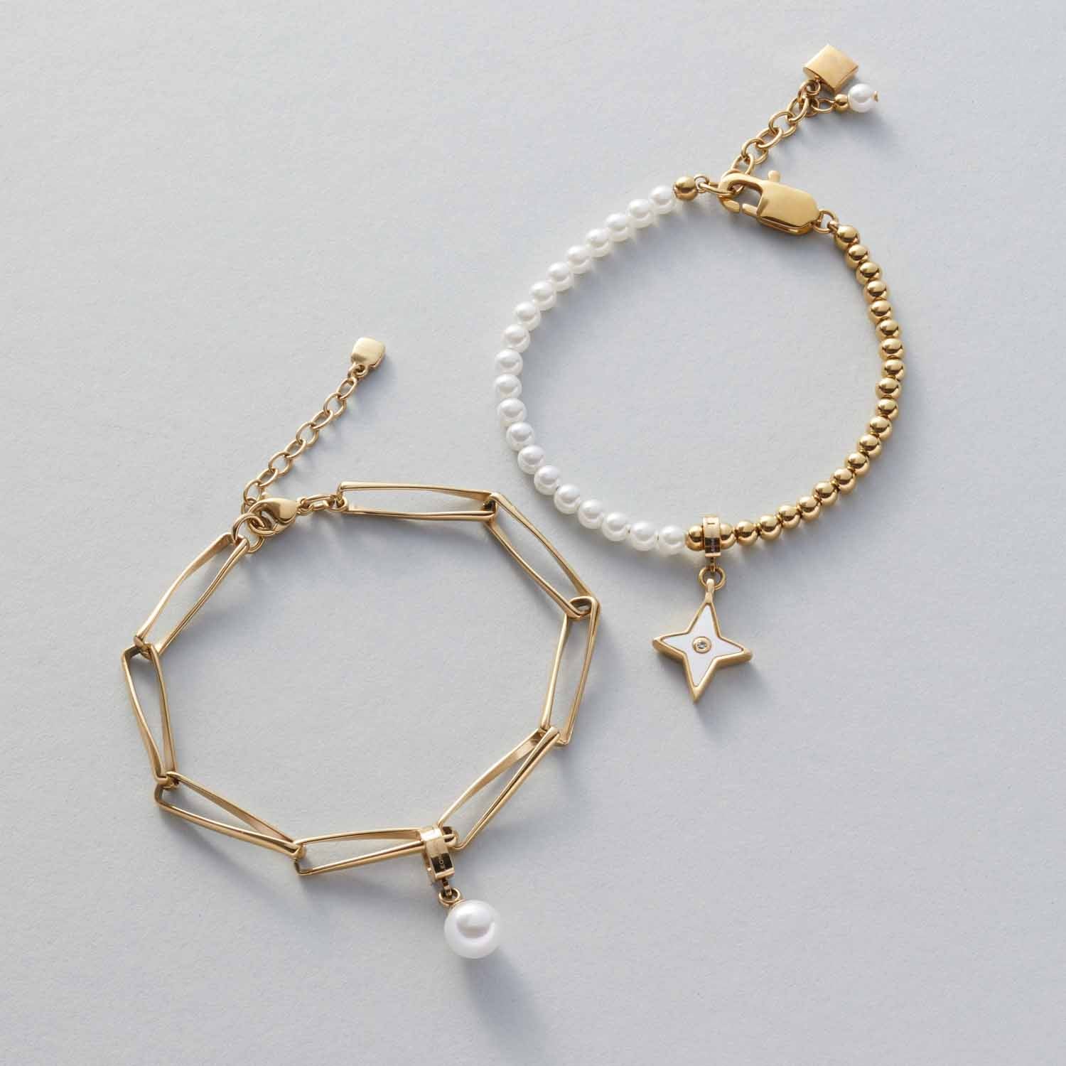 Zwei goldene Armbänder mit Perlen und Anhängern auf grauem Untergrund