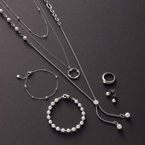 Silberschmuck mit Perlen: Halsketten, Armbänder und Ring auf grauem Untergrund