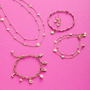 Goldene Schmuckkollektion mit Halsketten, Armbändern und Ohrringen auf rosa Hintergrund