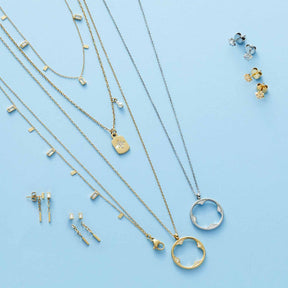 Schmuckkollektion auf hellblauem Untergrund: Halsketten, Ohrringe und Ohrhänger LIORA in Gold und Silber
