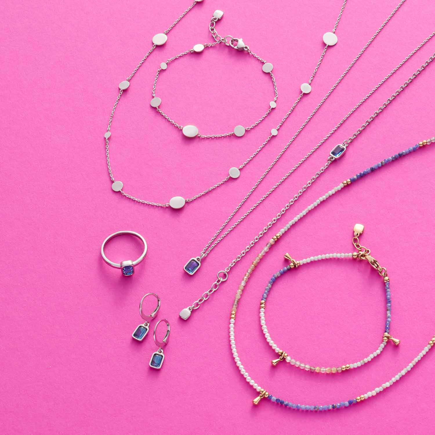 Schmuckkollektion auf rosa Hintergrund mit Halsketten, Armbändern und Ringen aus Edelstahl, Sodalith und Muscheln