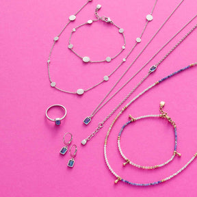 Schmuckkollektion auf rosa Hintergrund mit Halsketten, Armbändern und Ringen aus Edelstahl, Sodalith und Muscheln