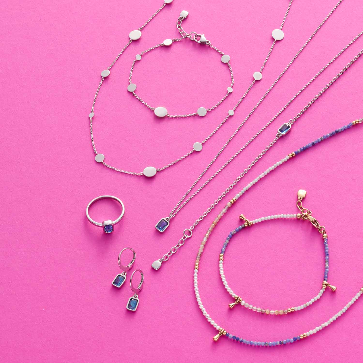 Schmuckkollektion auf rosa Untergrund: Halsketten, Armband und Ring aus Glas in Blau- und Weisstönen