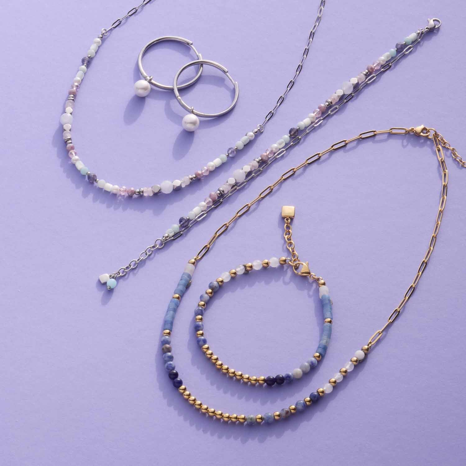 Armband BELINDA gold mit Glasperlen, Ringe und Ketten auf violettem Hintergrund
