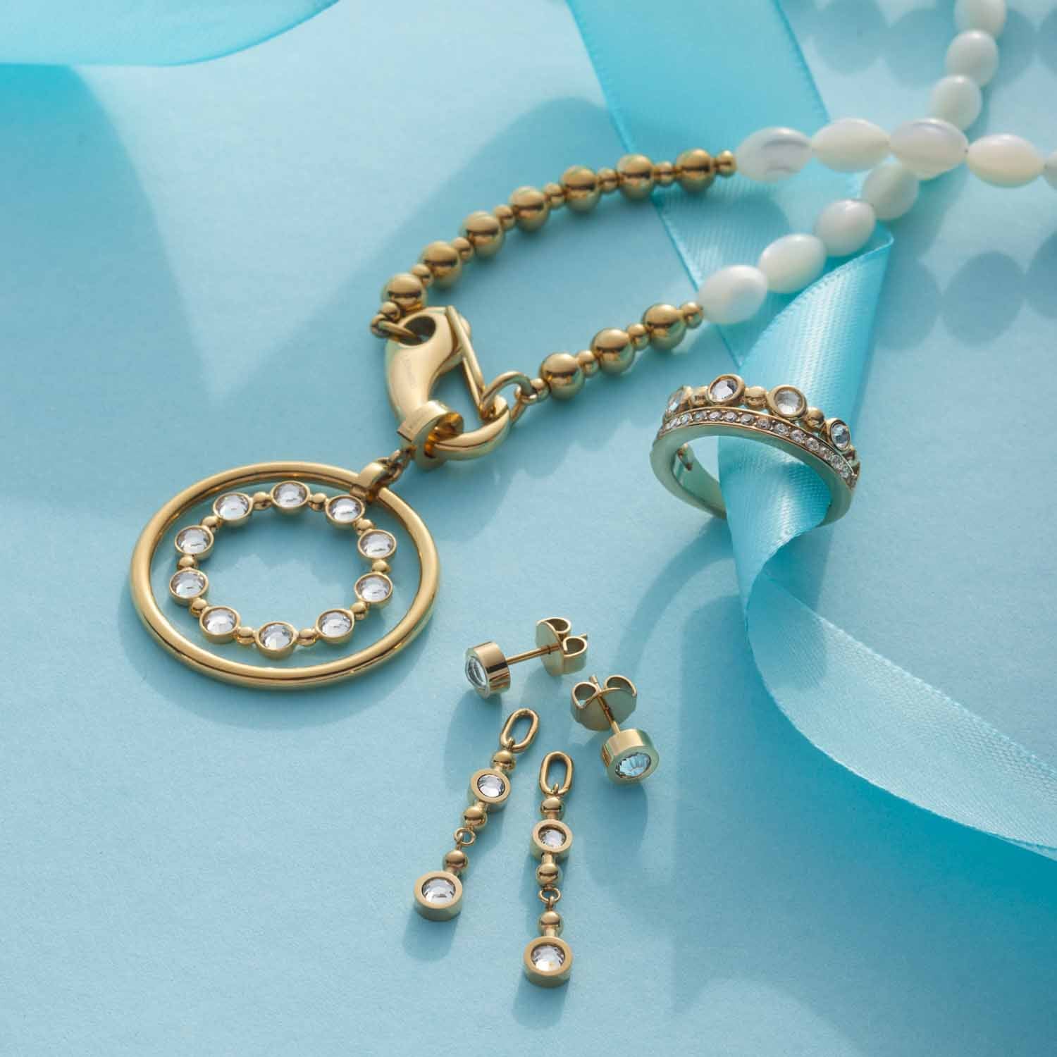 Halskette PATSY mit Anhänger, Ring und Ohrhänger auf blauem Untergrund