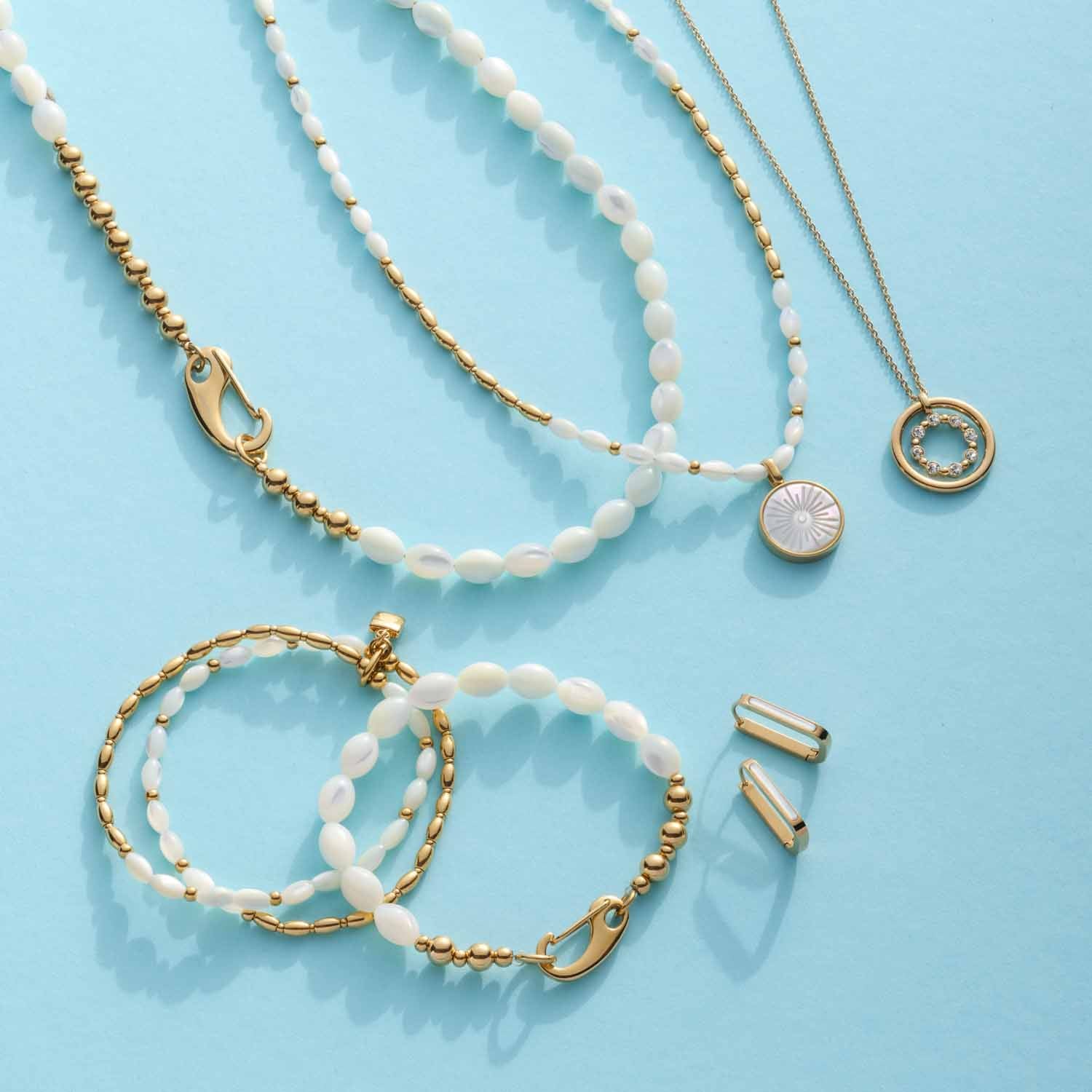 Armband PATSY gold mit Muschelelementen, Halsketten und Accessoires auf blauem Hintergrund