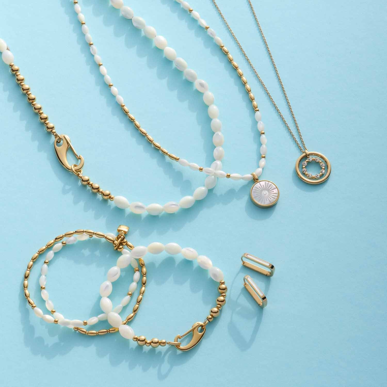 Armbänder und Halsketten aus Muscheln und goldfarbenen Elementen auf hellblauem Hintergrund