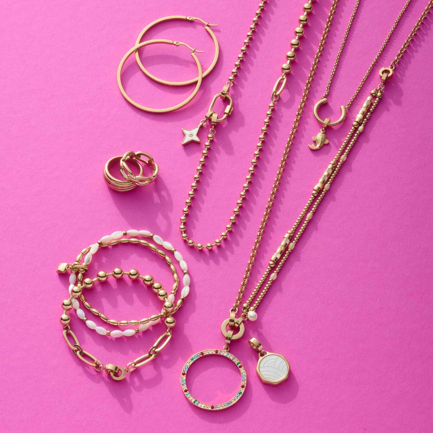 Goldene Schmuckkollektion mit Armbändern, Ringen und Halsketten auf rosa Hintergrund