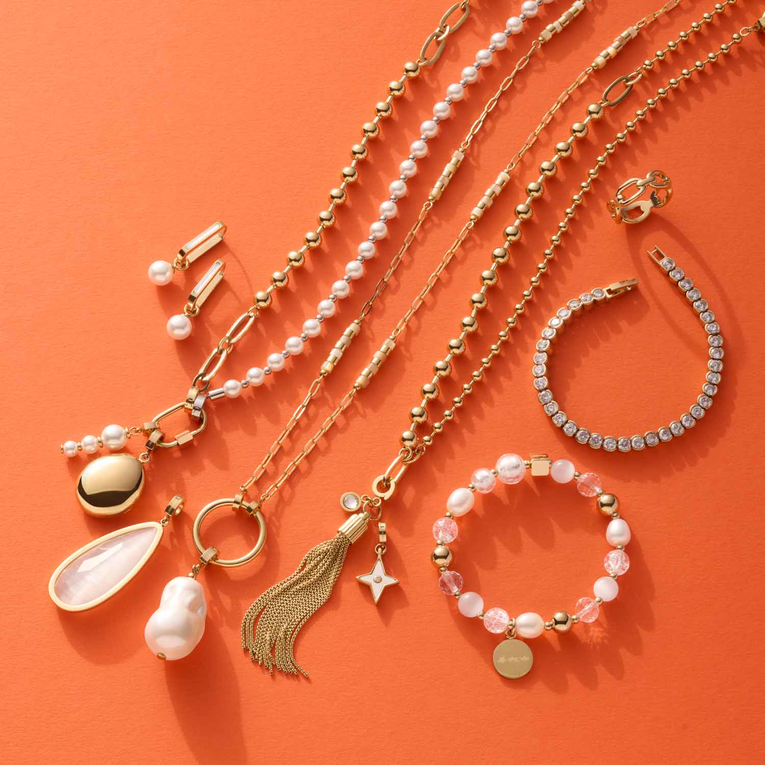 Schmuckkollektion auf orangefarbenem Hintergrund: Ketten, Creolen, Armbänder und Ohrringe mit Perlen und Muscheln