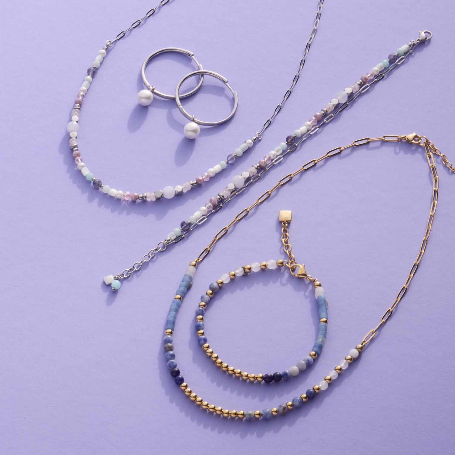 Schmuckkollektion mit Armbändern, Ringen und Ketten in Silber- und Goldtönen auf violettem Hintergrund