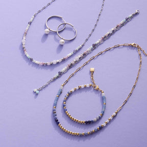 Schmuckkollektion mit Armbändern, Ringen und Ketten in Silber- und Goldtönen auf violettem Hintergrund