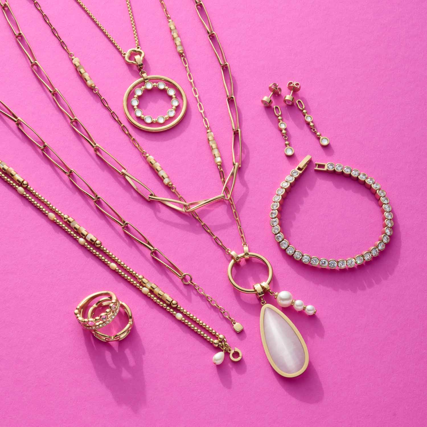 Schmuckkollektion mit Ketten, Ringen, Armband und Ohrhänger auf rosa Hintergrund