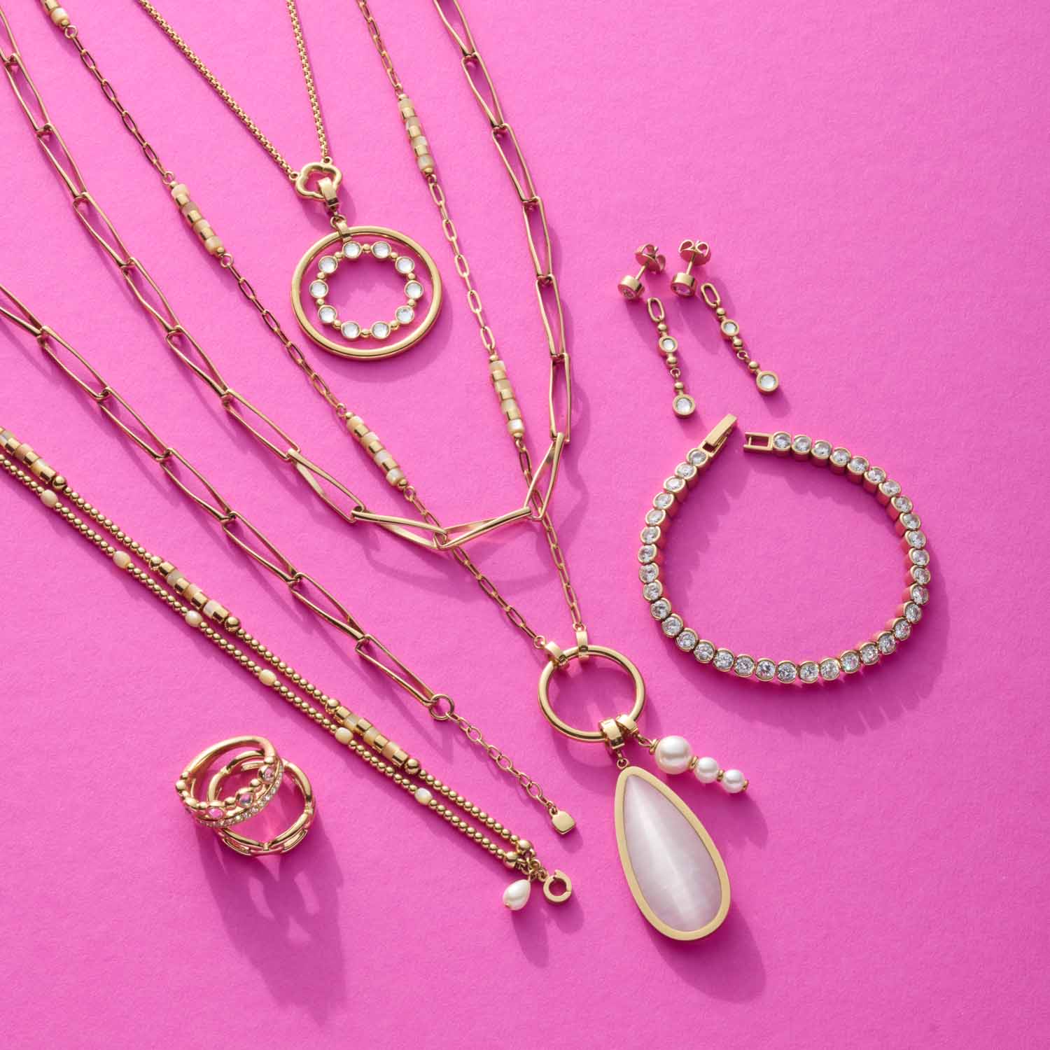 Goldene Schmuckkollektion auf pink: Halsketten, Armband, Ring und Ohrhänger BOBBY mit Zirkonia und Perlen