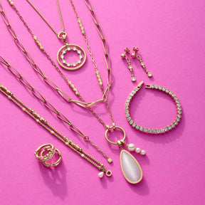 Goldene Schmuckkollektion auf pink: Halsketten, Armband, Ring und Ohrhänger BOBBY mit Zirkonia und Perlen