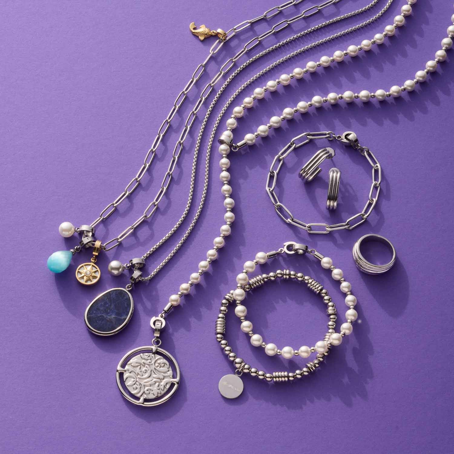 Schmuckkollektion mit Ketten, Armbändern und Ring auf violettem Hintergrund
