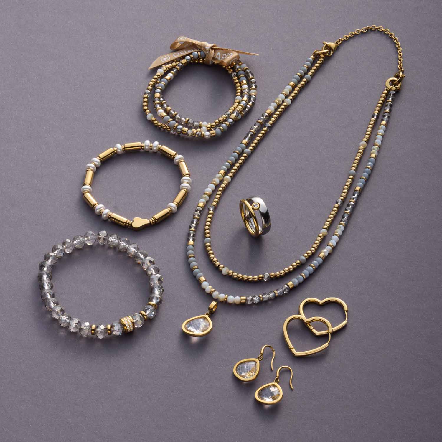 Armband BERNADETTE gold mit weiteren Schmuckteilen und Glasperlen auf grauem Hintergrund