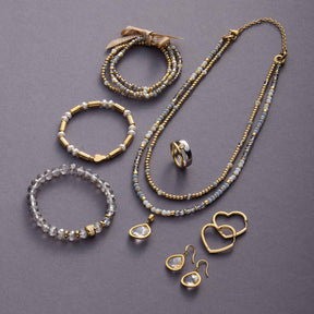 Armband BERNADETTE gold mit weiteren Schmuckteilen und Glasperlen auf grauem Hintergrund