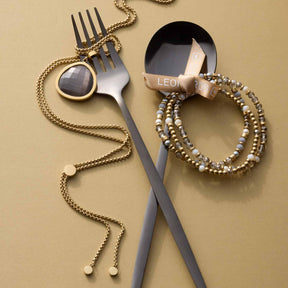 Armband BERNADETTE gold mit Besteck und Schmuck auf beigem Hintergrund