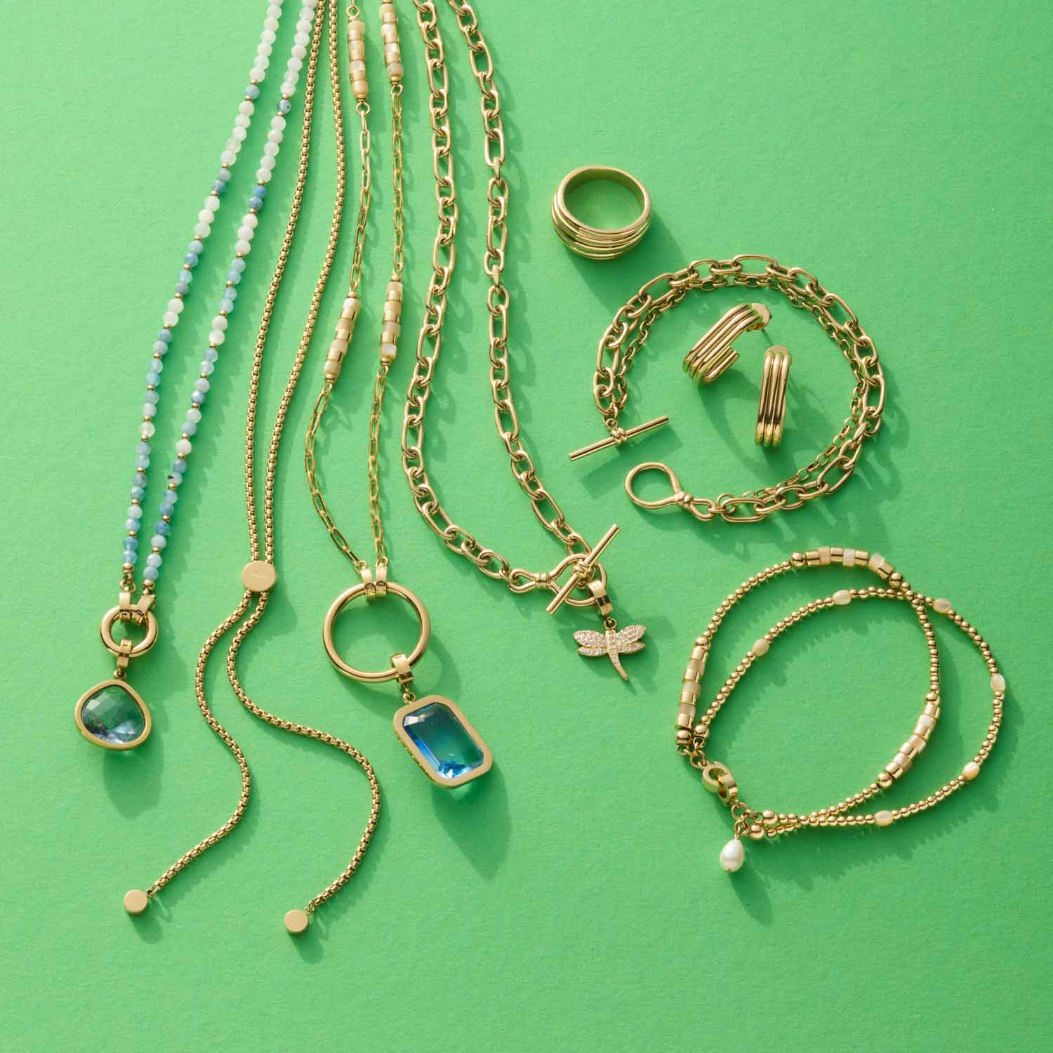 Goldene Ketten, Armbänder und Ohrringe auf grünem Hintergrund