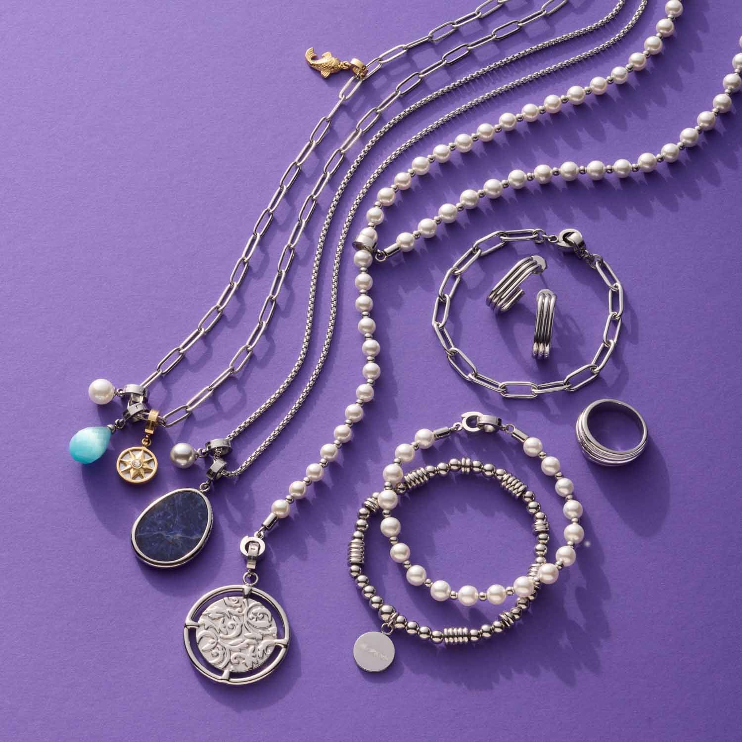Schmuckkollektion auf violettem Hintergrund mit Ketten, Armbändern und Ringen in Silber