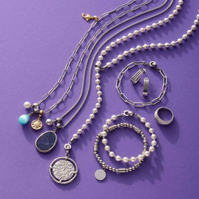 Schmuckkollektion auf violettem Hintergrund mit Ketten, Armbändern und Ringen in Silber