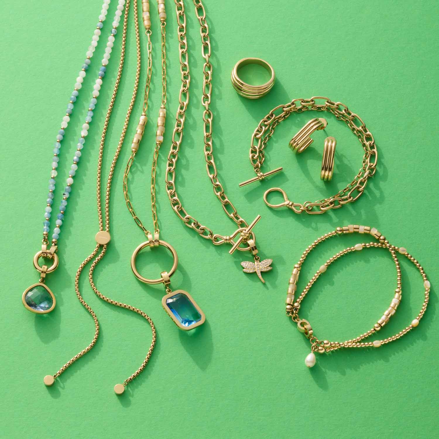 Schmuckkollektion aus goldenen Ketten, Ringen, Armbändern und Ohrringen auf grünem Hintergrund
