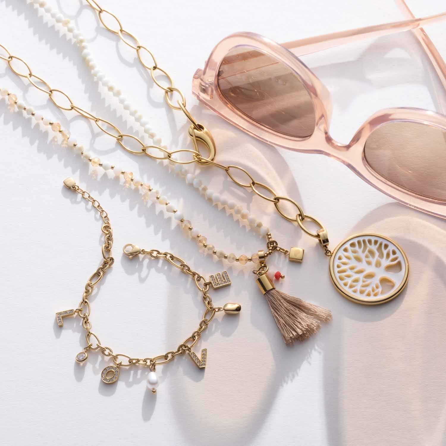 Halskette DONNA mit Glasperlen, Goldkette und Charm-Anhängern, Sonnenbrillen und Deko-Objekt auf weißem Untergrund