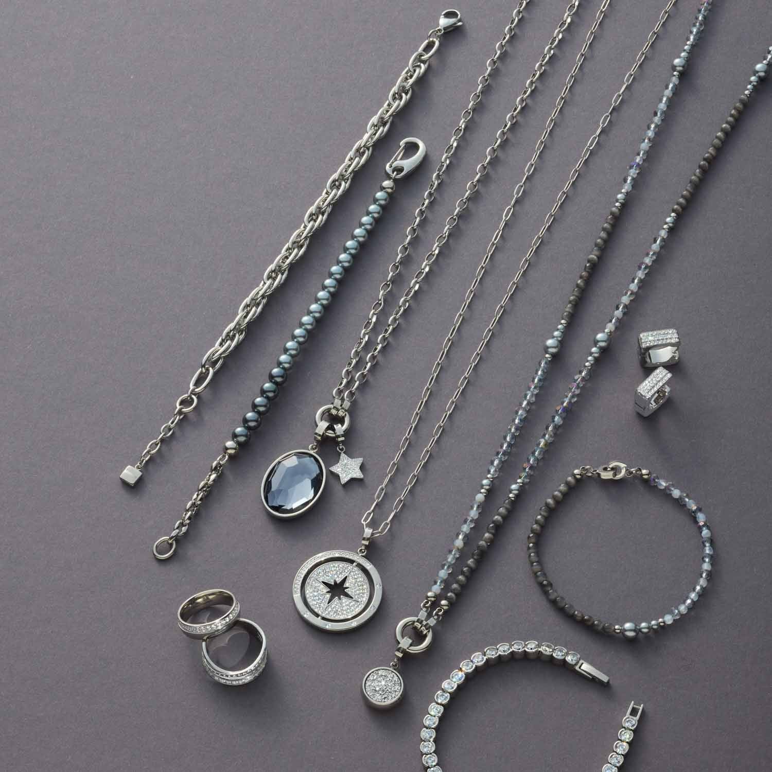 Schmuckkollektion mit Ketten, Ringen und Armbändern aus Edelstahl auf grauem Hintergrund