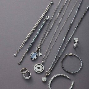Schmuckkollektion mit Ketten, Ringen und Armbändern aus Edelstahl auf grauem Hintergrund